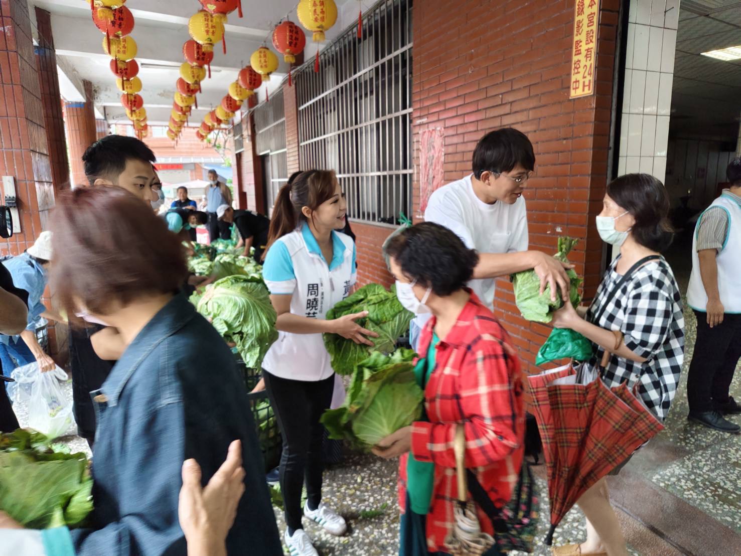 黃國昌在廟前廣場主持「公益發送高麗菜,一人一顆挺菜農」活動,周曉芸從旁搭下手協助。(圖/民眾黨立院黨團)
