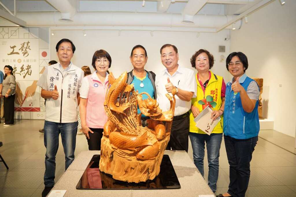 ▲新竹縣副縣長陳見賢(右三)欣賞曾文魁(左三)老師的木雕作品「力爭上游五福臨門」。