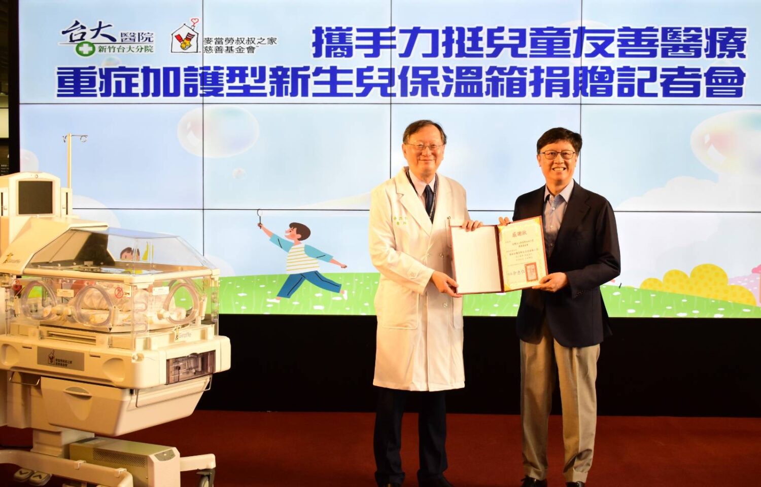 新竹臺大分院院長余忠仁(左)代表受贈,感謝麥當勞叔叔之家慈善基金會董事長李昌霖(右)捐贈兩台重症加護型新生兒保溫箱,攜手提升早產與重症新生兒照護品質。(圖/記者張家燁翻攝)