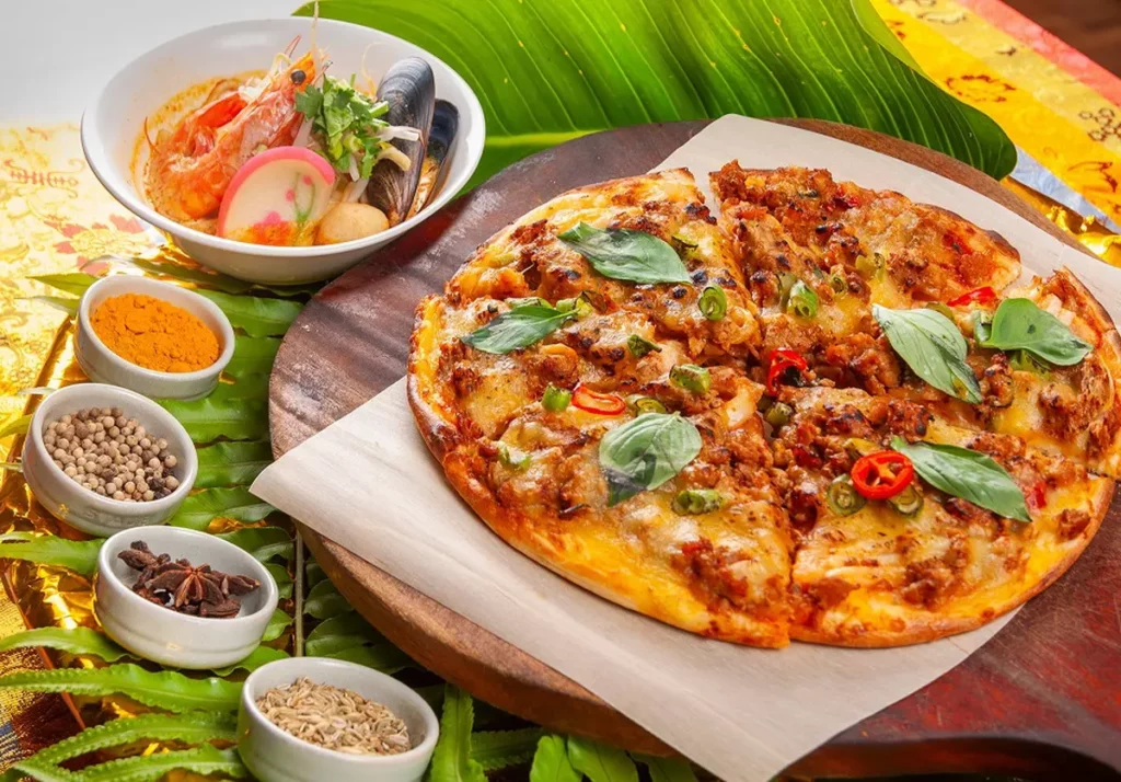 現煮「南洋叻沙麵」(左)湯頭辛香,入口微帶椰香甜味;「打拋豬肉披薩」(右)將經典熱炒搬上餅皮,是令人驚喜的東西合璧創意之作。/台北凱撒大飯店提供