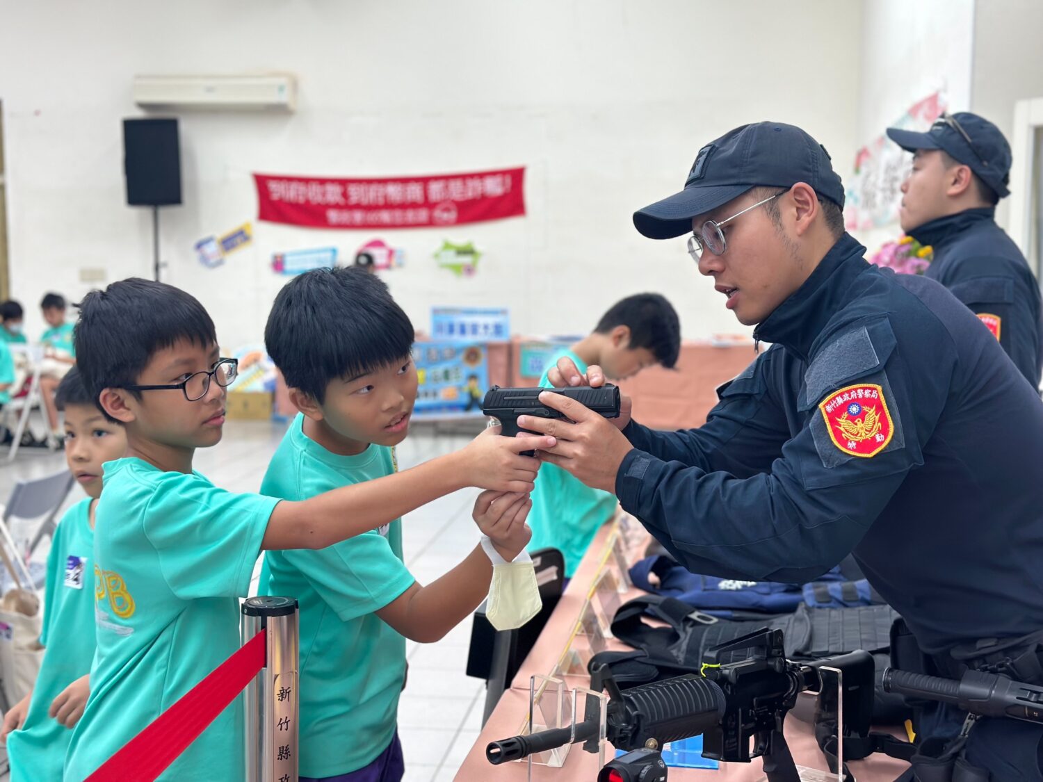 新竹縣警察局霹靂小組警員向學生們介紹警用手槍操作,學生興奮體驗射擊模擬,感受真實警察裝備的震撼。(圖/記者張家燁翻攝)