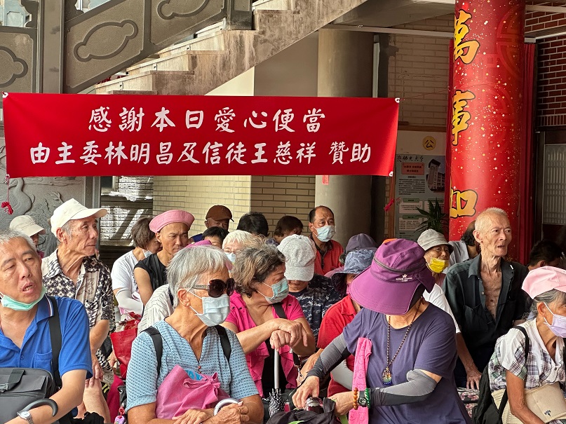 ▲五穀廟擴大愛心便當發放,現場懸掛本日由主委林明昌及王慈祥贊助布條。