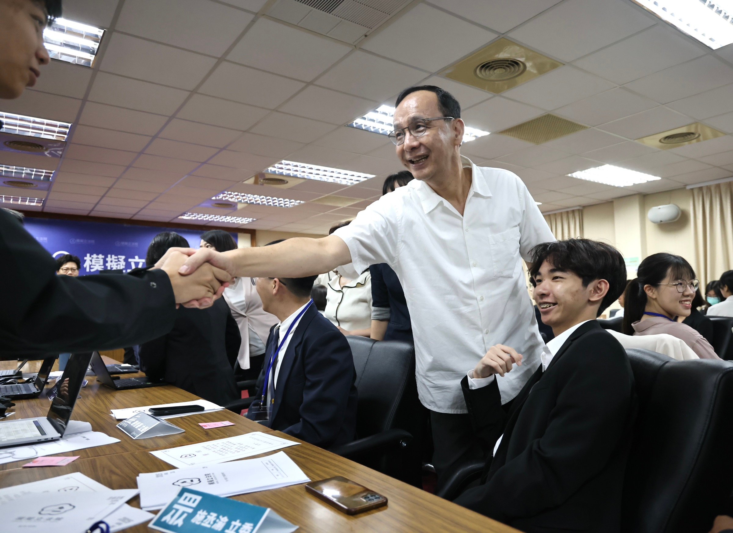 國民黨主席朱立倫26日上午出席2025模擬立法院開幕式,活動前與學員握手互動國民黨主朱立倫(前左)26日上午出席2025模擬立法院開幕式。林啟弘攝