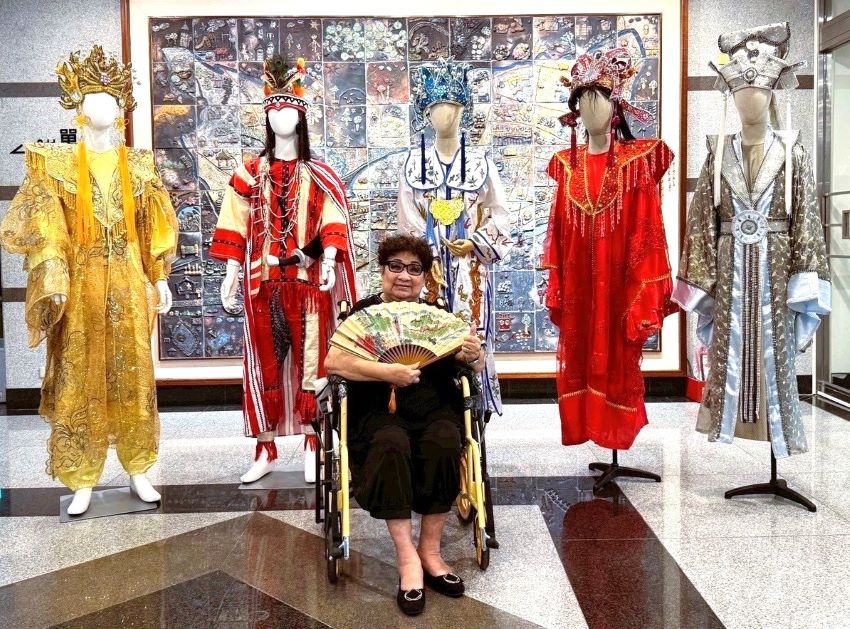 新莊文藝中心《明雪璀璨映戲臺》 洪明雪藝師特展 1 《圖說》「2025新莊有好戲」系列活動,今日起於新莊文化藝術中心推出《明雪璀璨映戲臺──藝師洪明雪片段記事》特展,圖為洪明雪藝師與她親手縫製、實際穿戴過的戲服。〈文化局提供〉