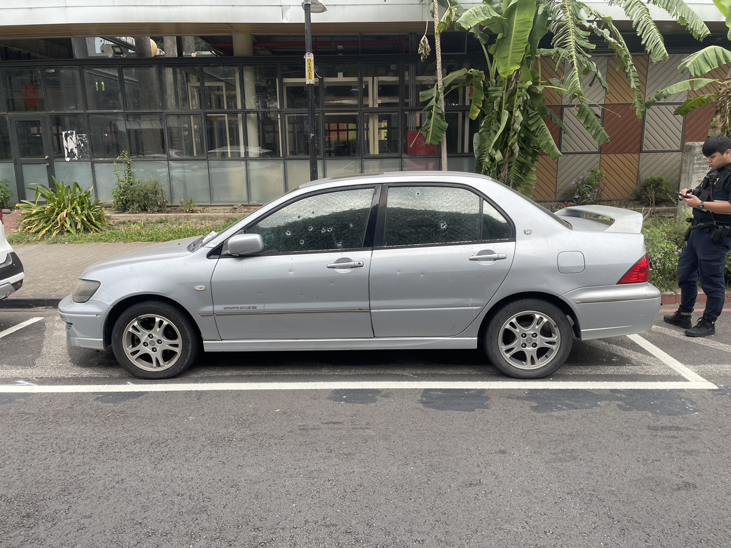 1輛停放在學校附近的銀色轎車,車身和玻璃佈滿了多處彈孔。