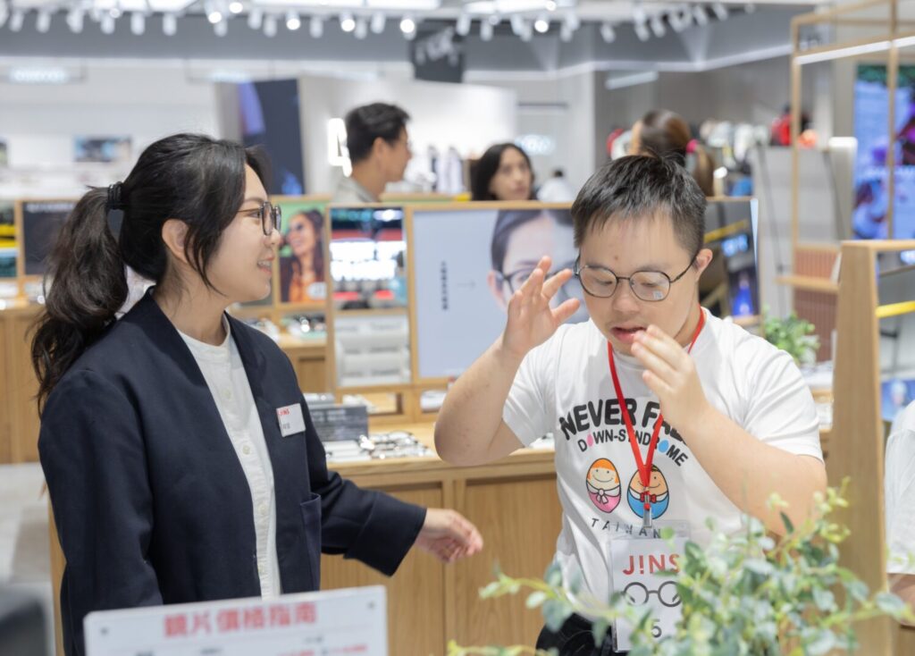 JINS 舉辦公益配鏡活動，門市人員陪同唐氏症青年挑選並試戴眼鏡。（圖／主辦單位提供）