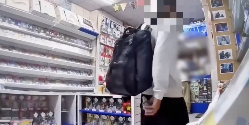 男子將店內展示櫃內之PS5手把放入後背包與衣服之間的影像截圖。(圖/記者 趙靜姸翻攝)