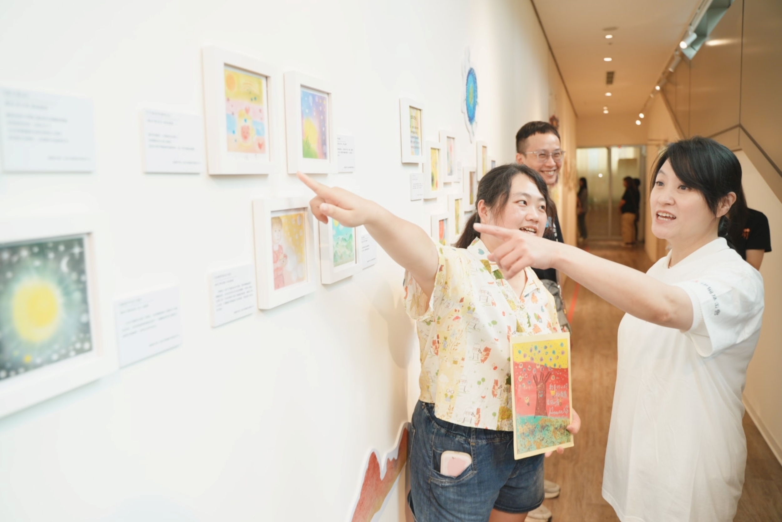 伊甸基金會邀早療家庭、身心障礙者創作 《光從心底升起》聯展桃園總圖登場 伊甸公益大使海芬與慢飛天使鈞鈞媽媽,一同欣賞慢飛天使及身心障礙朋友的作品。伊甸基金會提供