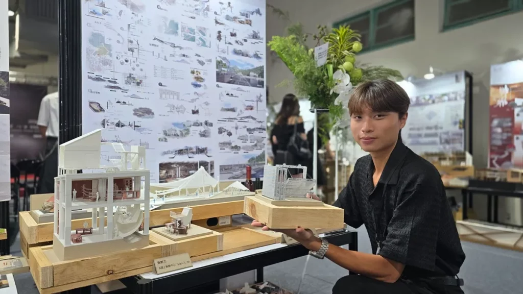 學生林峻民以作品〈漁創力〉翻轉漁港想像，他手持模型搶魚平台，說明當地下午5點漁船進港後「搶魚」的傳統商業特色，為此設計出可移動式的分流平台。這不僅能避免魚貨在拍賣過程中受損，更能讓遊客與居民擁有更優質的「搶魚體驗」。（圖/陳惠玲攝影）