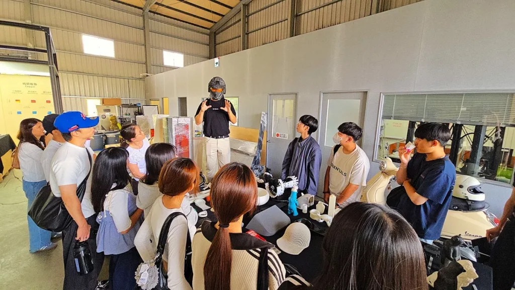 朝陽科技大學工業設計系校友李旻宸,他頭戴自家設計的3D列印安全帽,說明桌上展示的設計作品的故事。(圖/陳惠玲攝影)