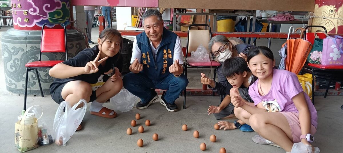 ▲高雄東照山關帝廟端午節立蛋活動吸引親子家庭熱情參與，主委潘献有（中）與大小朋友一同挑戰立蛋，分享端午好運與平安祝福，現場洋溢歡樂溫馨的節慶氛圍。