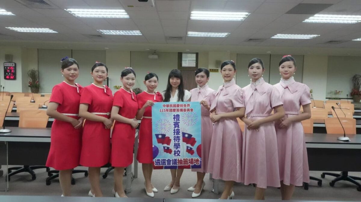 ▲崇仁專校美容保健科師生於「115年國慶禮賓接待學校遴選會議抽籤場地」現場合影。蔡伊媜主任(中)帶領穿著紅、粉兩色優雅禮賓服的團員們共同亮相，團隊洋溢著自信微笑與端莊儀態，展現出崇仁美保科齊心協心、全力以赴爭取國家級慶典服務榮譽的團隊凝聚力。
