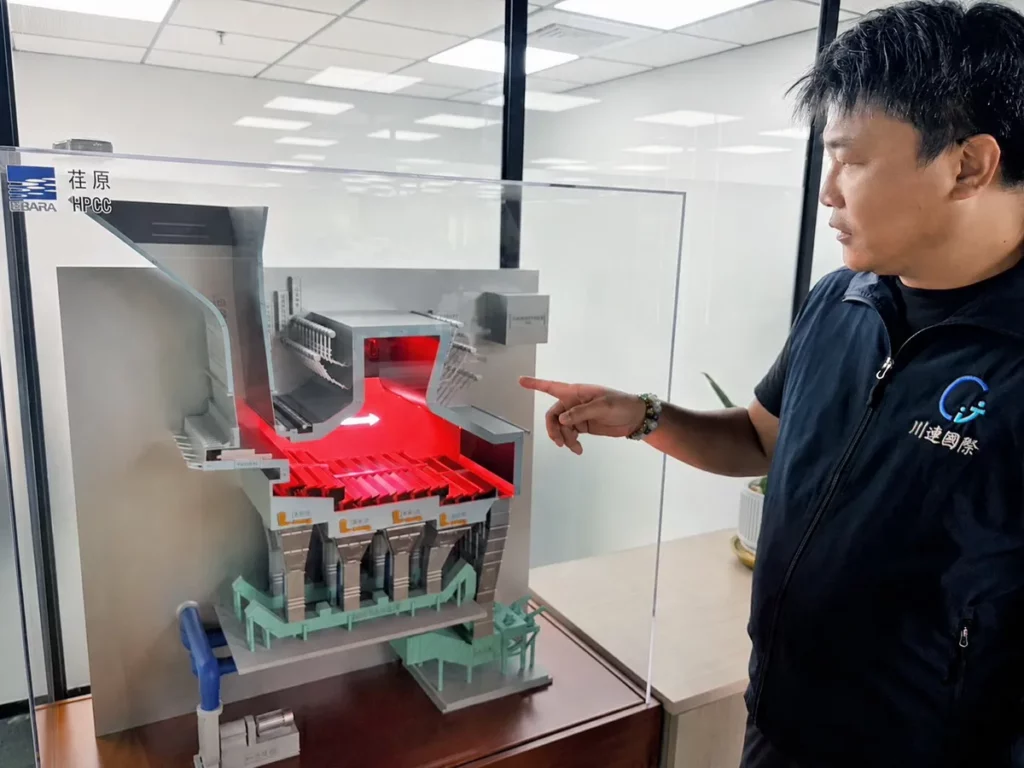 川連國際總經理翁三裕於荏原（EBARA）展示的焚化系統剖面模型前，講解爐體內部燃燒與熱能傳導機制。圖片來源：川連國際