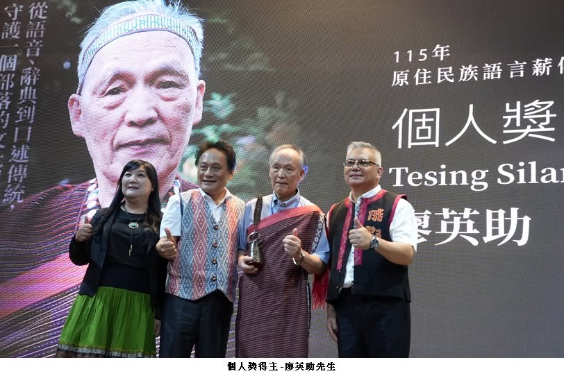 可能是一或多人、講臺和顯示的文字是「到 傳 115年 原住民族語言薪 個人獎 Tesing TesingSila Sila 英助 魔 個人獎得主-廖英助先生 個人獎得主 摩英助先生」的圖像