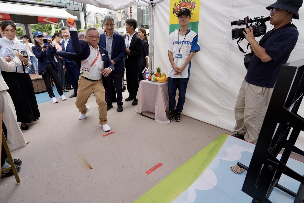 行政院政務委員吳誠文(前)於園遊會體驗區嘗試九宮格投擲遊戲,透過趣味互動向日本民眾推廣臺灣農產品。圖/農業部提供